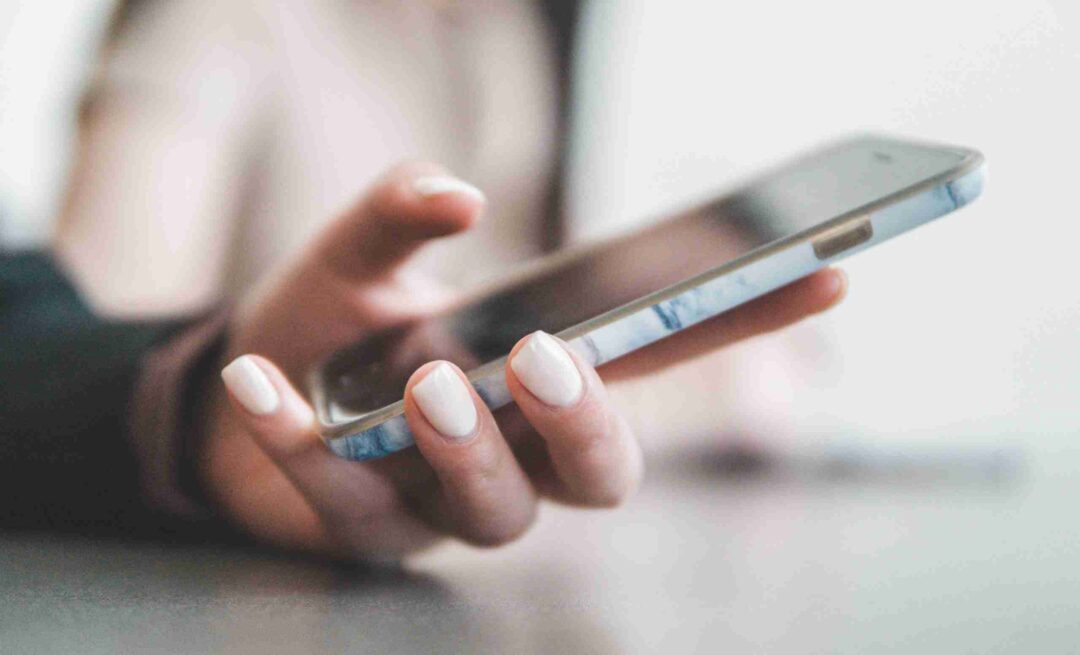 Close-up of a person holding a smartphone with white-painted nails
