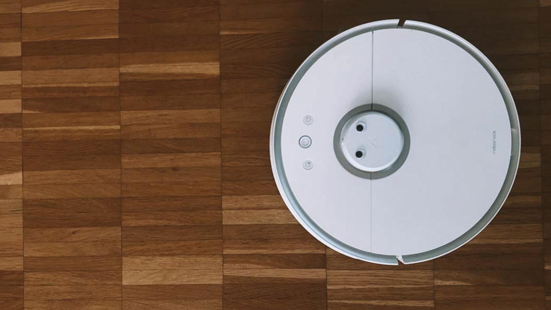 White robotic vacuum cleaner on a wooden floor viewed from above