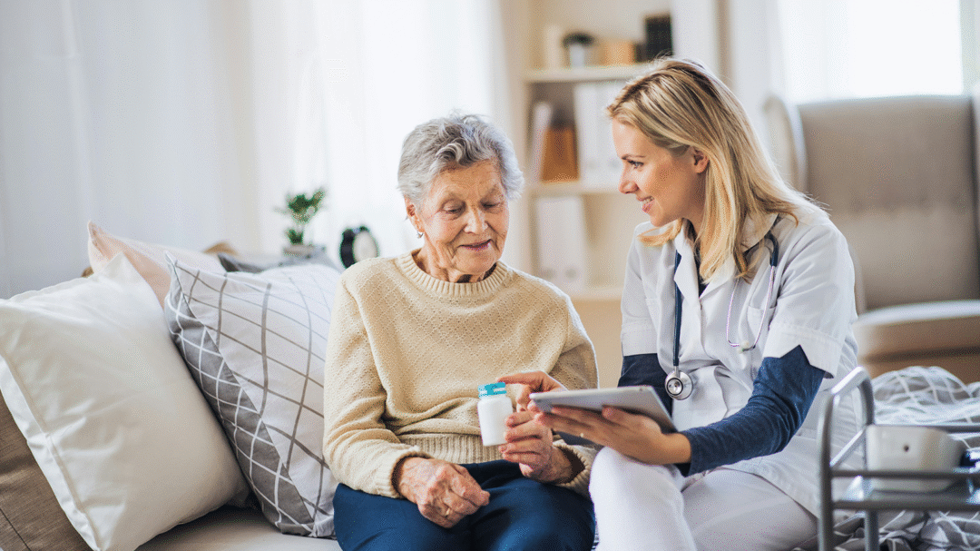 Nellie Supports professional discussing medication with an elderly patient while seated on a sofa