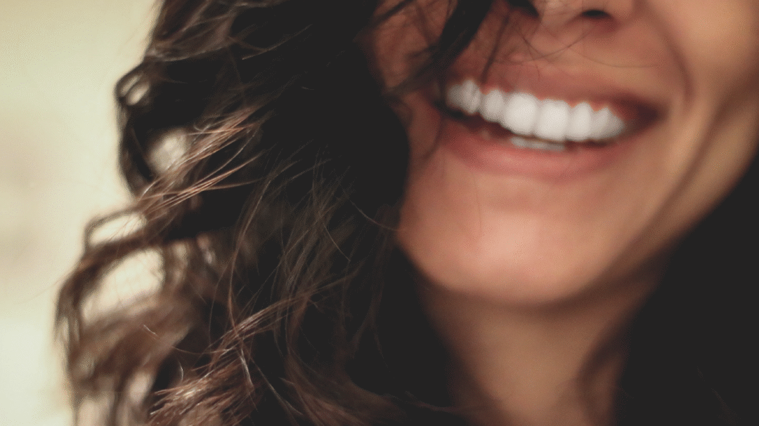 Close-up of a person smiling with bright white teeth and wavy hair partially covering their face
