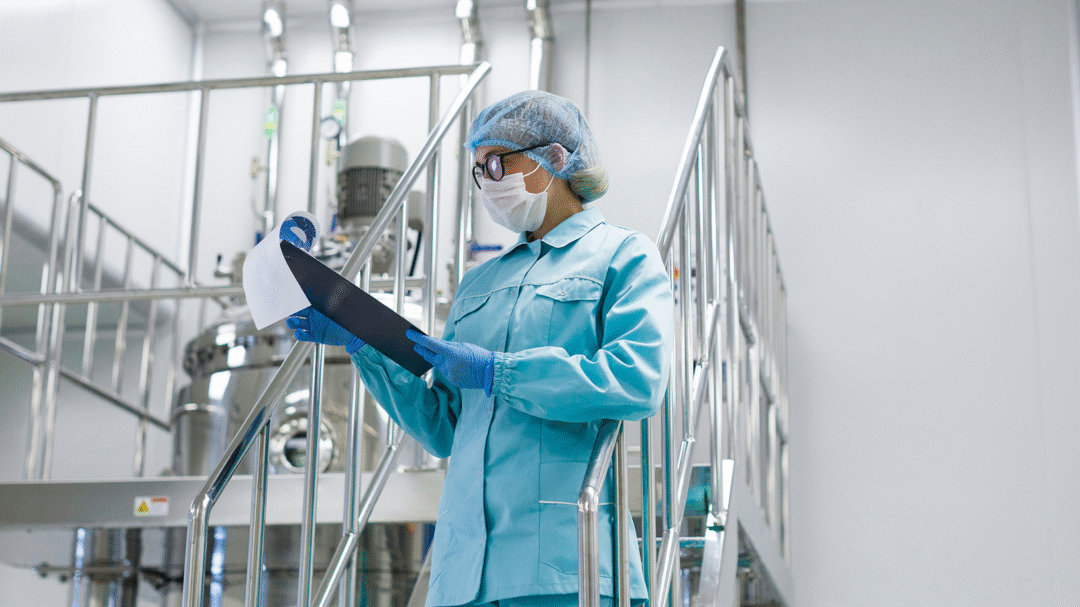 Technician wearing protective cleanroom clothing reviewing documents inside a controlled manufacturing environment, representing Cleanroom Shop’s specialist equipment and supplies