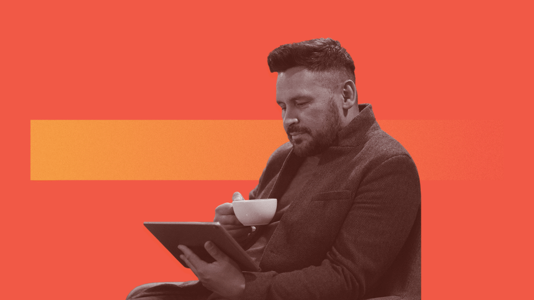 A man drinking a cup of tea while looking at a tablet