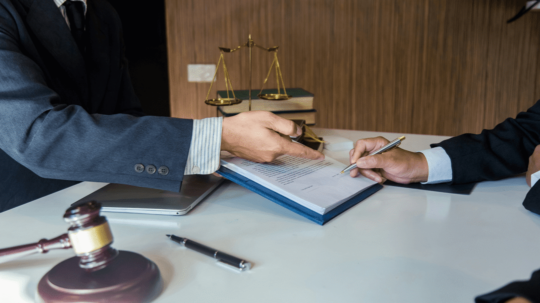 Two professionals reviewing and signing a legal document with a gavel and scales of justice on the desk