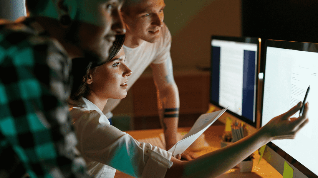 Team of digital marketers working together at computer screens in a dimly lit office