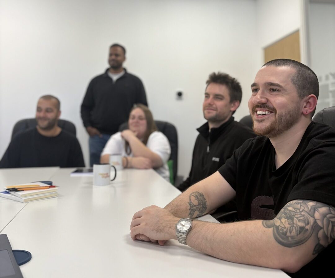 Team of five colleagues smiling and listening during a meeting in a bright office conference room